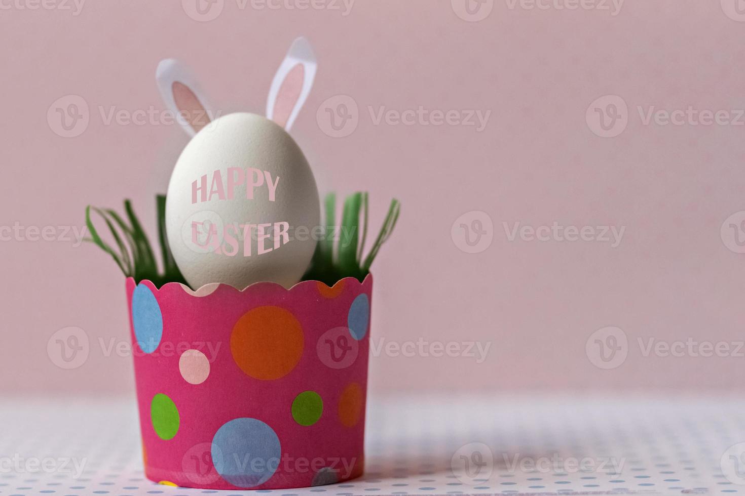 huevo de gallina blanco con orejas de conejo en una bandeja de papel rosa ecológico, caja. feliz concepto de vacaciones de pascua. texto en inglés felices pascuas foto