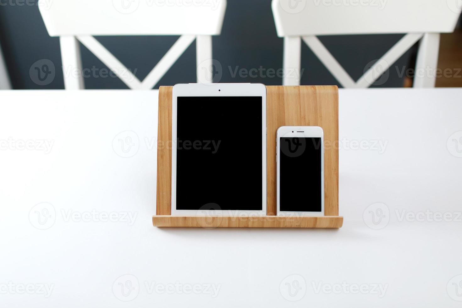 a white tablet and a smartphone with a black screen on a stand on a white table. office workplace photo