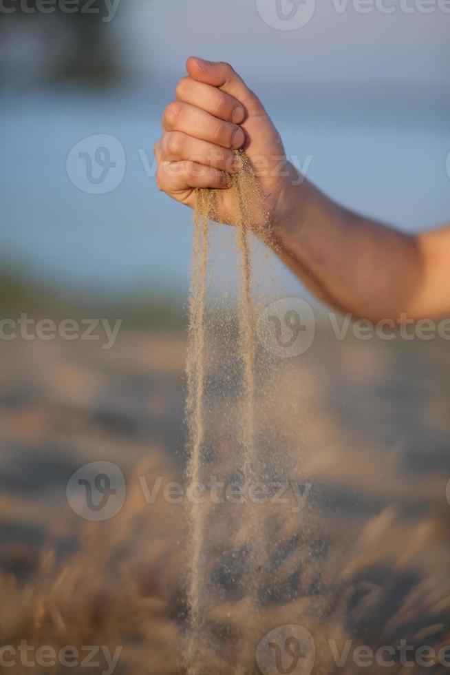 arena que fluye a través de las manos contra el océano azul. mano de primer plano que suelta la arena que cae. concepto de playa de verano foto