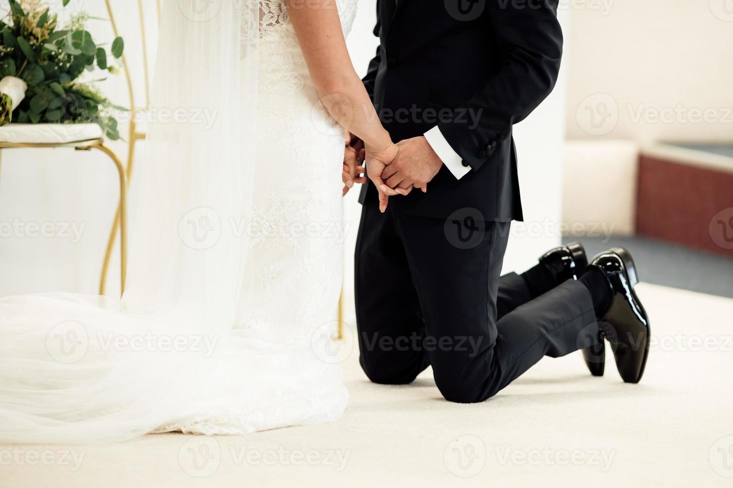 newlyweds standing on their knees holding hands and closed their eyes. selective focus. photo