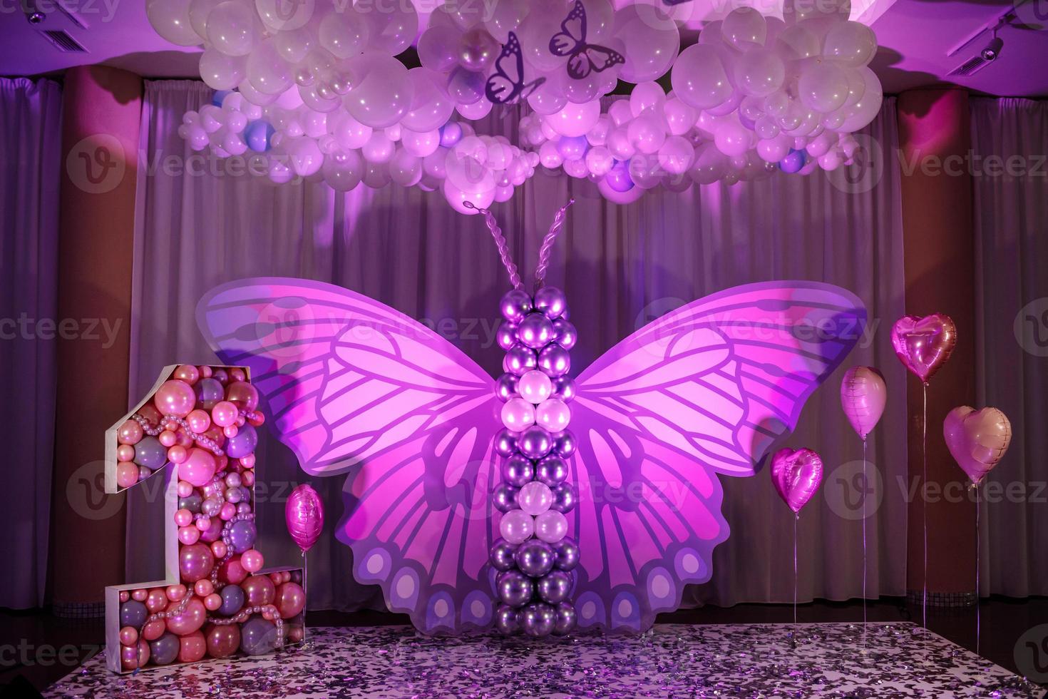 Decor of the girl's first birthday. Beautiful pink photo zone for one year old baby girl with big paper and balls butterfly. big letter number one with pink balloons. Happy Birthday party