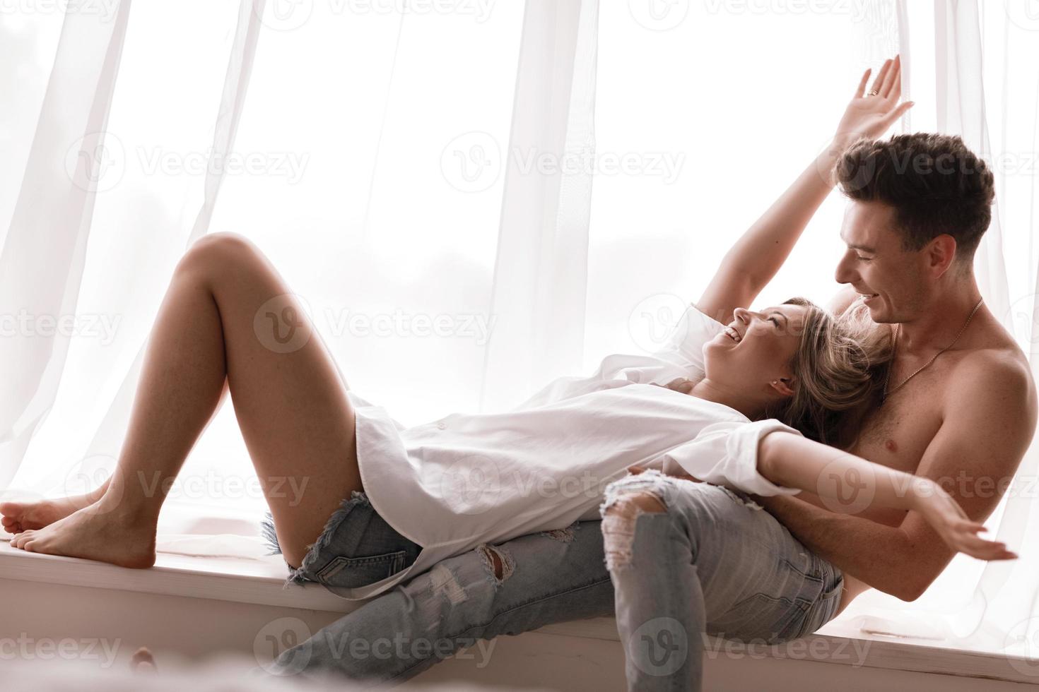 loving couple having fun together at home, playful wife biting smiling husband ear, piggyback, man and woman playing childish in bed, enjoying funny intimate moments photo