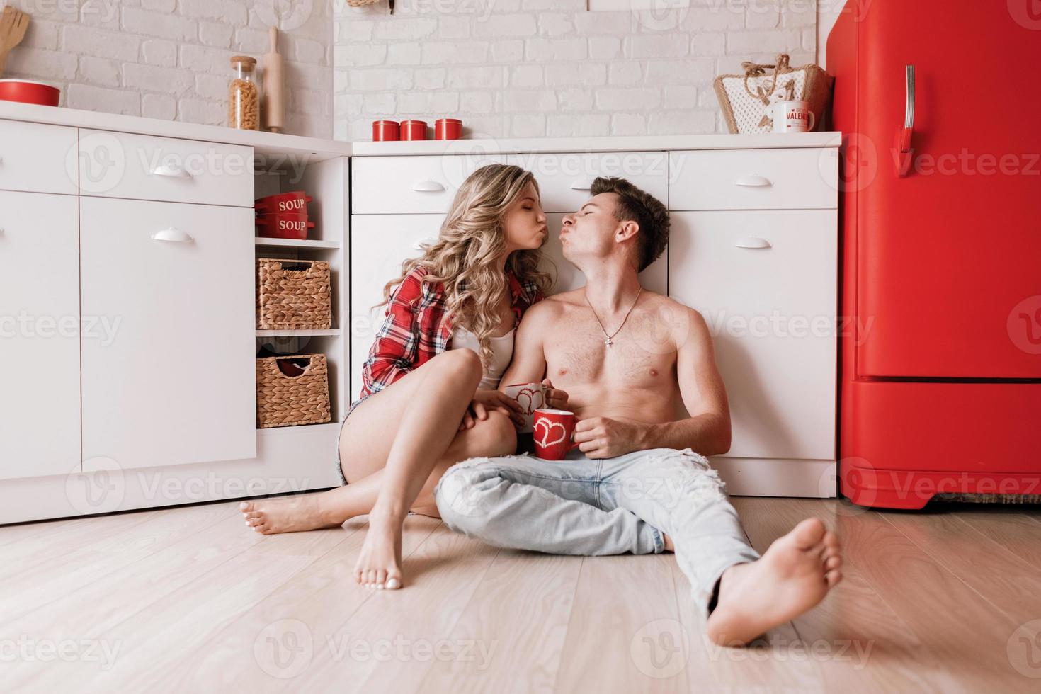 Lovely girl sitting on the floor and having fun with boyfriend. Young couple enjoying coffee or tea in the kitchen. photo