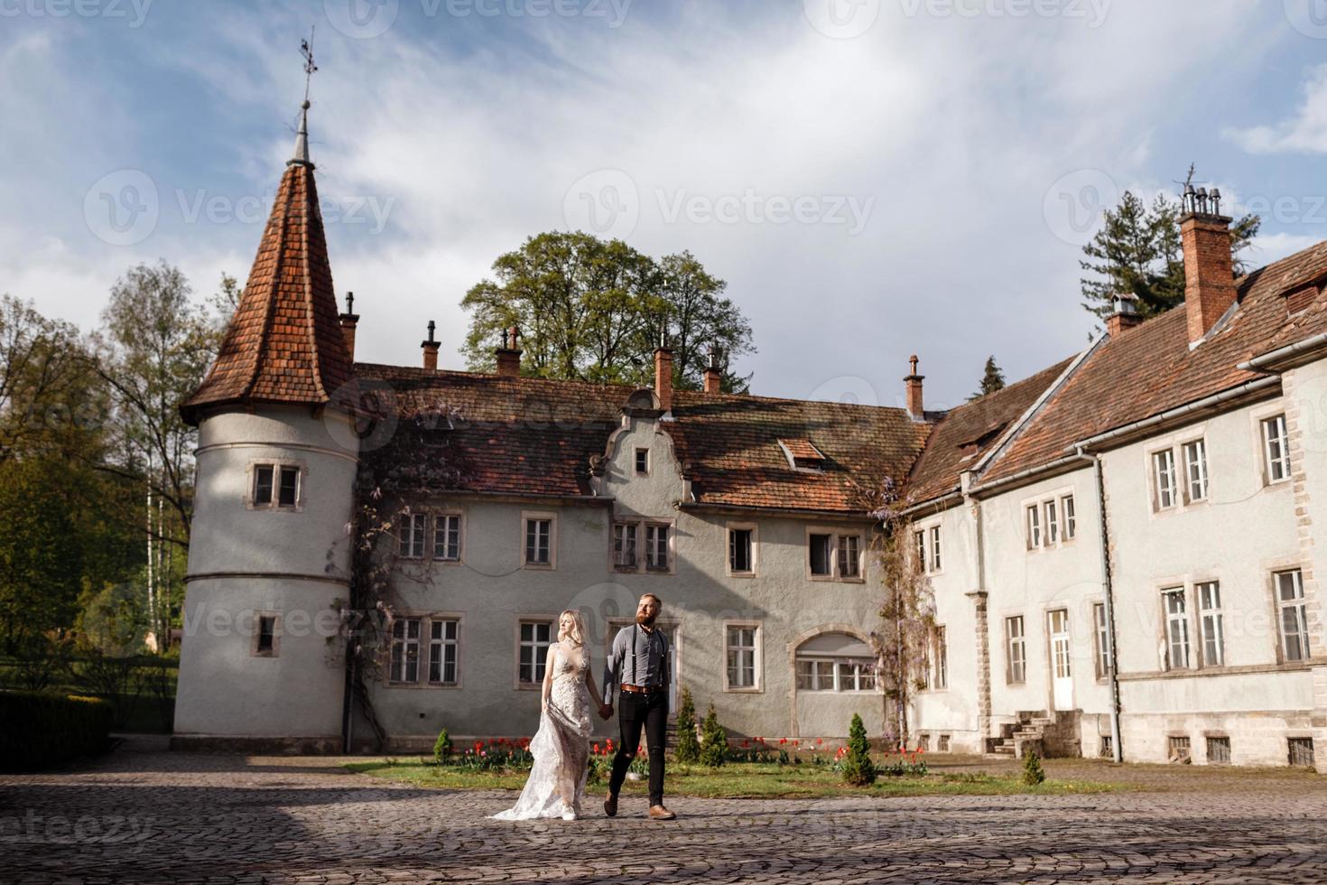 hermosos novios están caminando cerca del antiguo castillo, arquitectura antigua restaurada, edificio antiguo, casa vieja afuera, palacio vintage al aire libre. amor romántico en la calle de ambiente vintage foto