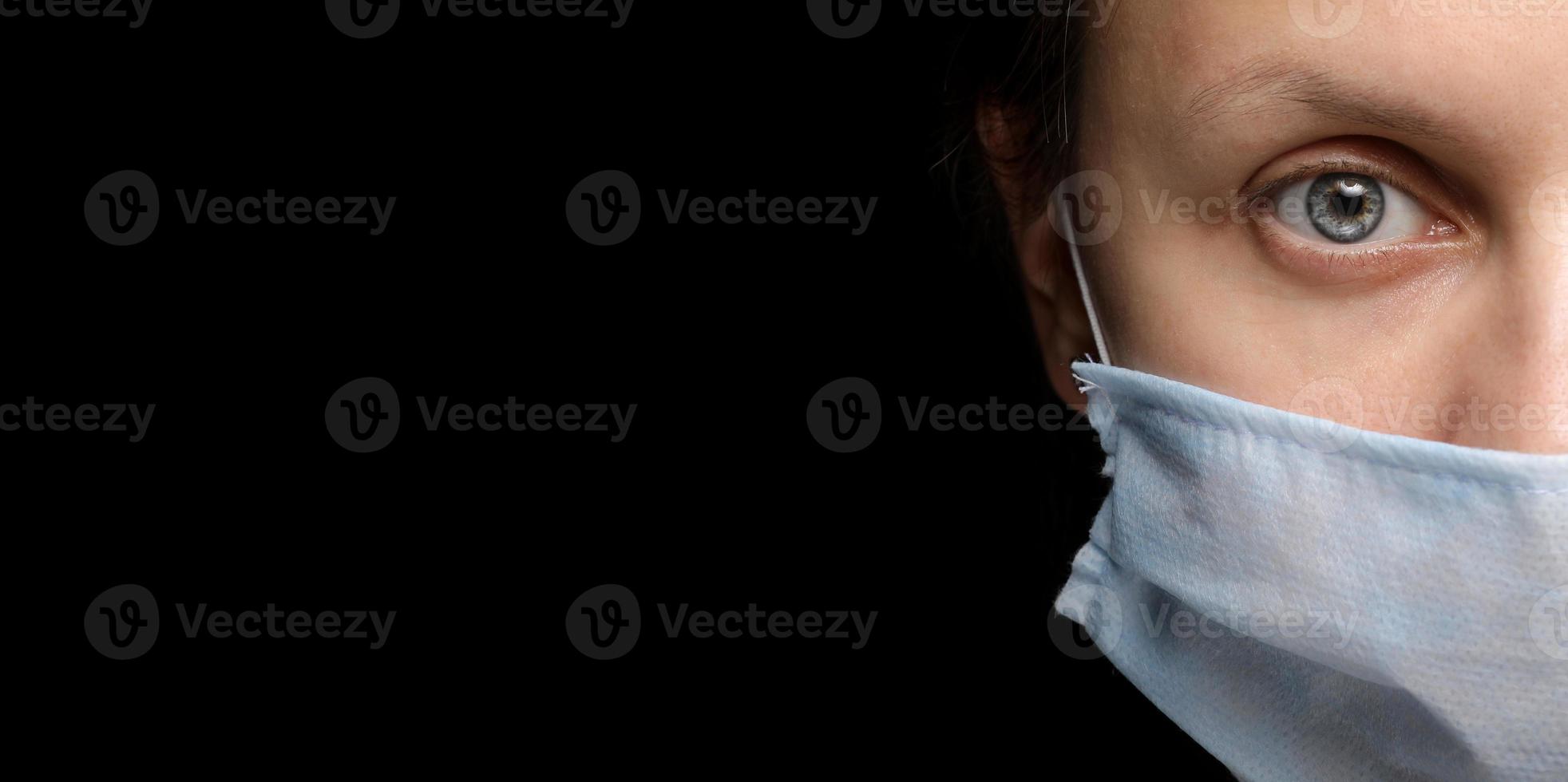 pancarta del rostro de una mujer con una máscara médica sobre fondo negro, un brote de infección por coronavirus y protección contra él. primer plano, retrato de estudio en una oscuridad. copia espacio, mira a la cámara foto