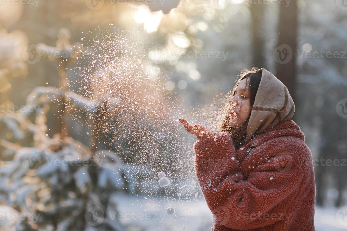 Beautiful, stylish and young girl, blowing the snow from her hands in winter forest. Christmas holiday. photo