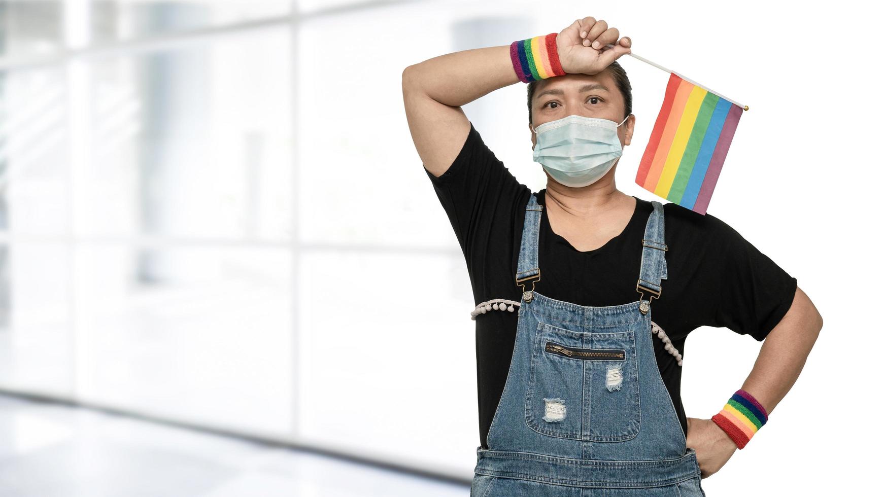 Asian lady wearing mask for protect covid-19 virus holding rainbow flag, symbol of LGBT pride month celebrate annual in June social of gay, lesbian, bisexual, transgender, human rights. photo