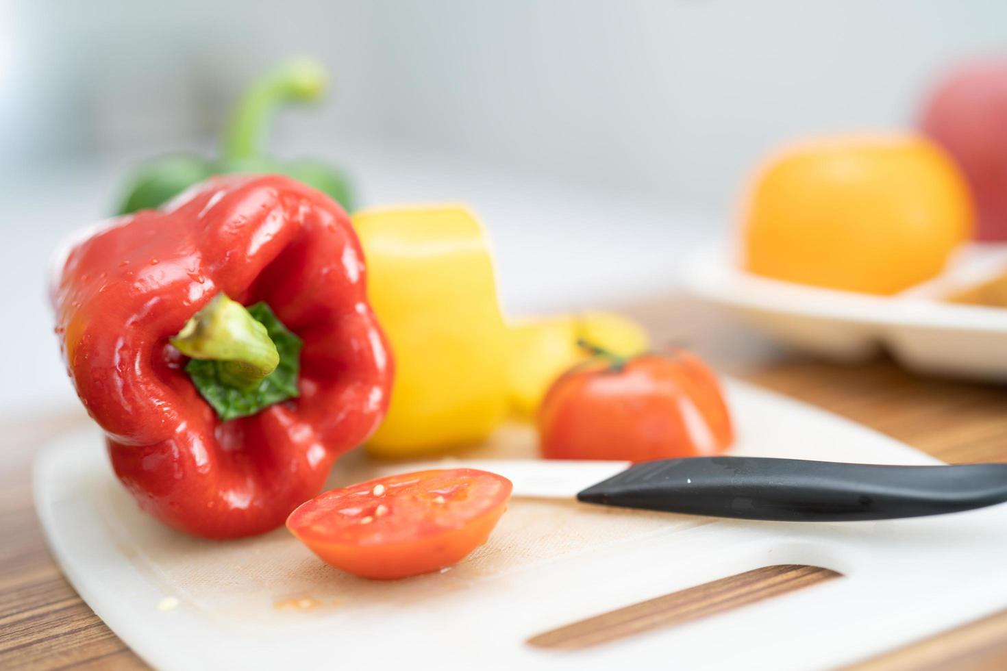 Pimiento rojo y tomate con un cuchillo en la tabla de cortar, ensalada de verduras, cocinar alimentos saludables foto