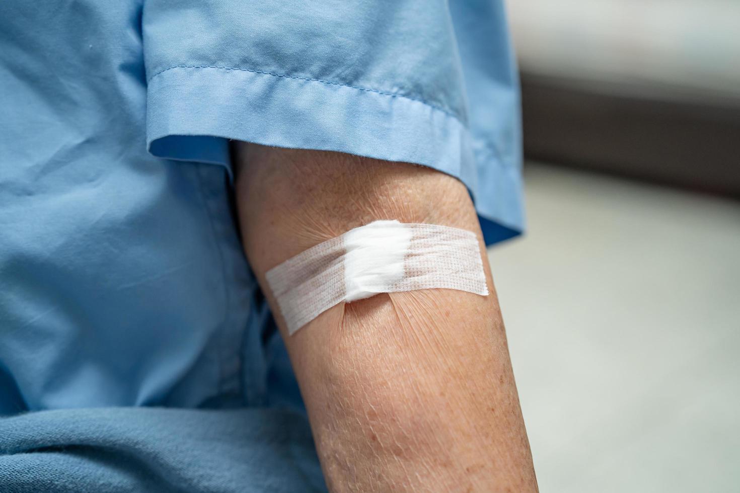 Asian senior or elderly old lady woman patient show cotton wool stop bleeding, after blood drawing testing for annually physical health check up to check cholesterol, blood pressure, and sugar level. photo