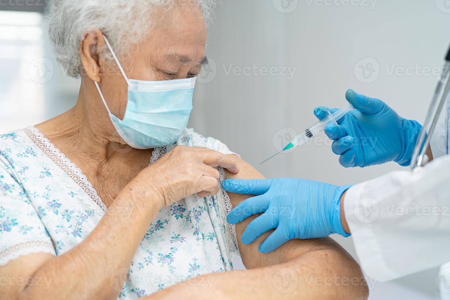 Elderly Asian senior woman wearing face mask getting covid-19 or coronavirus vaccine by doctor make injection. photo