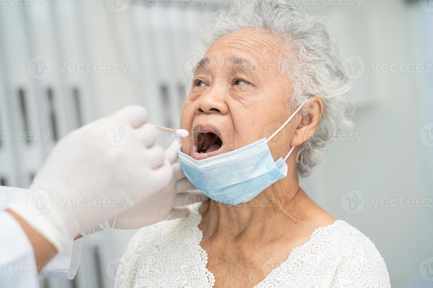 Doctor in pep suit taking a throat and nasal swab from senior asian woman patient to test covid-19 coronavirus infection. photo