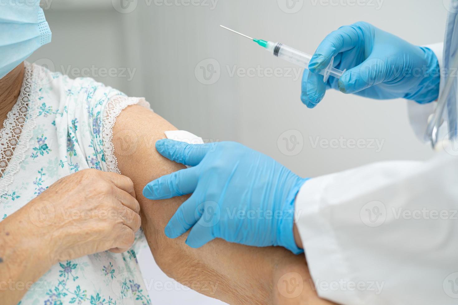 Elderly Asian senior woman wearing face mask getting covid-19 or coronavirus vaccine by doctor make injection. photo