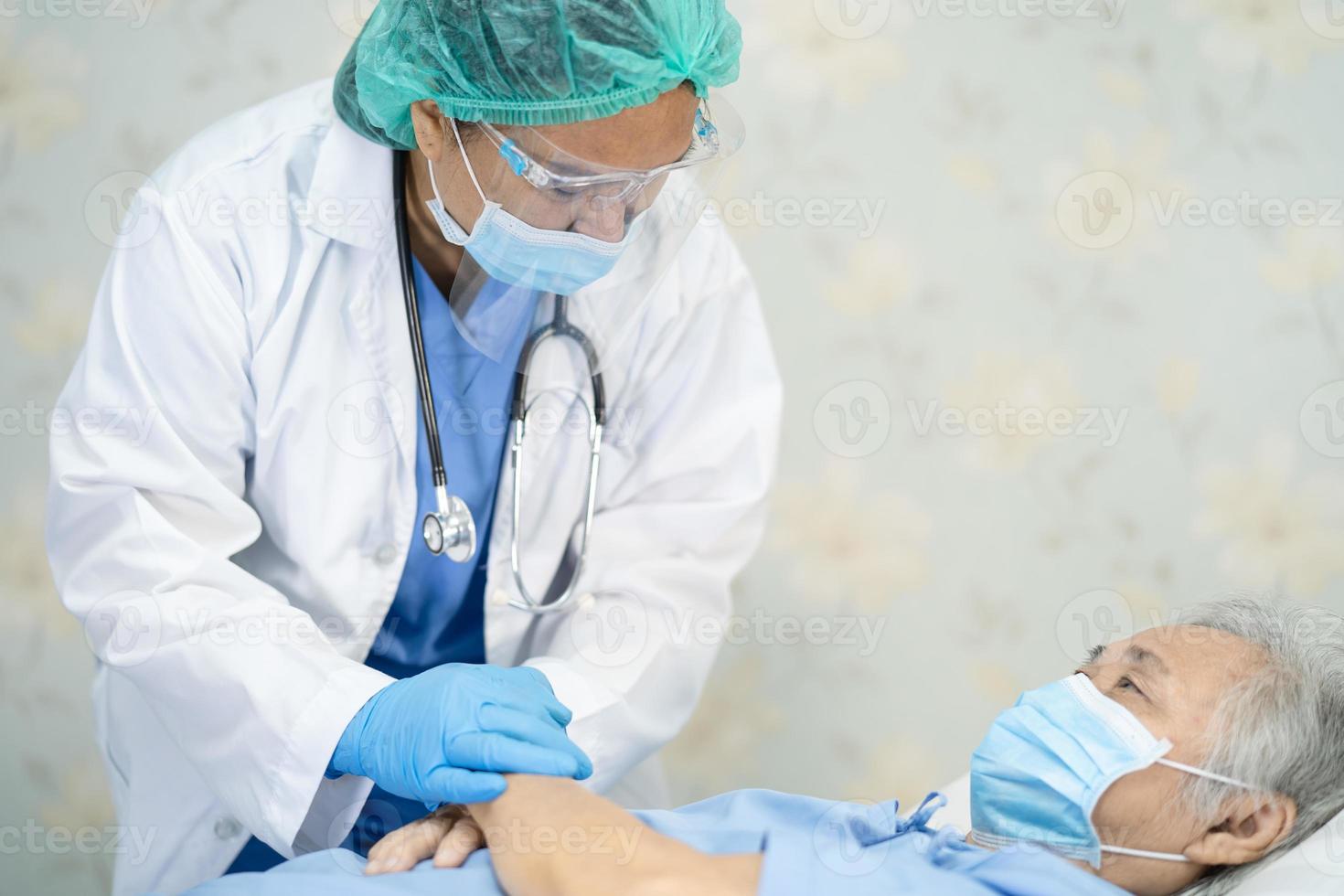 médico asiático con protector facial y traje de ppe nuevo normal para comprobar que el paciente protege la seguridad infección brote de coronavirus covid-19 en la sala de cuarentena del hospital de enfermería. foto