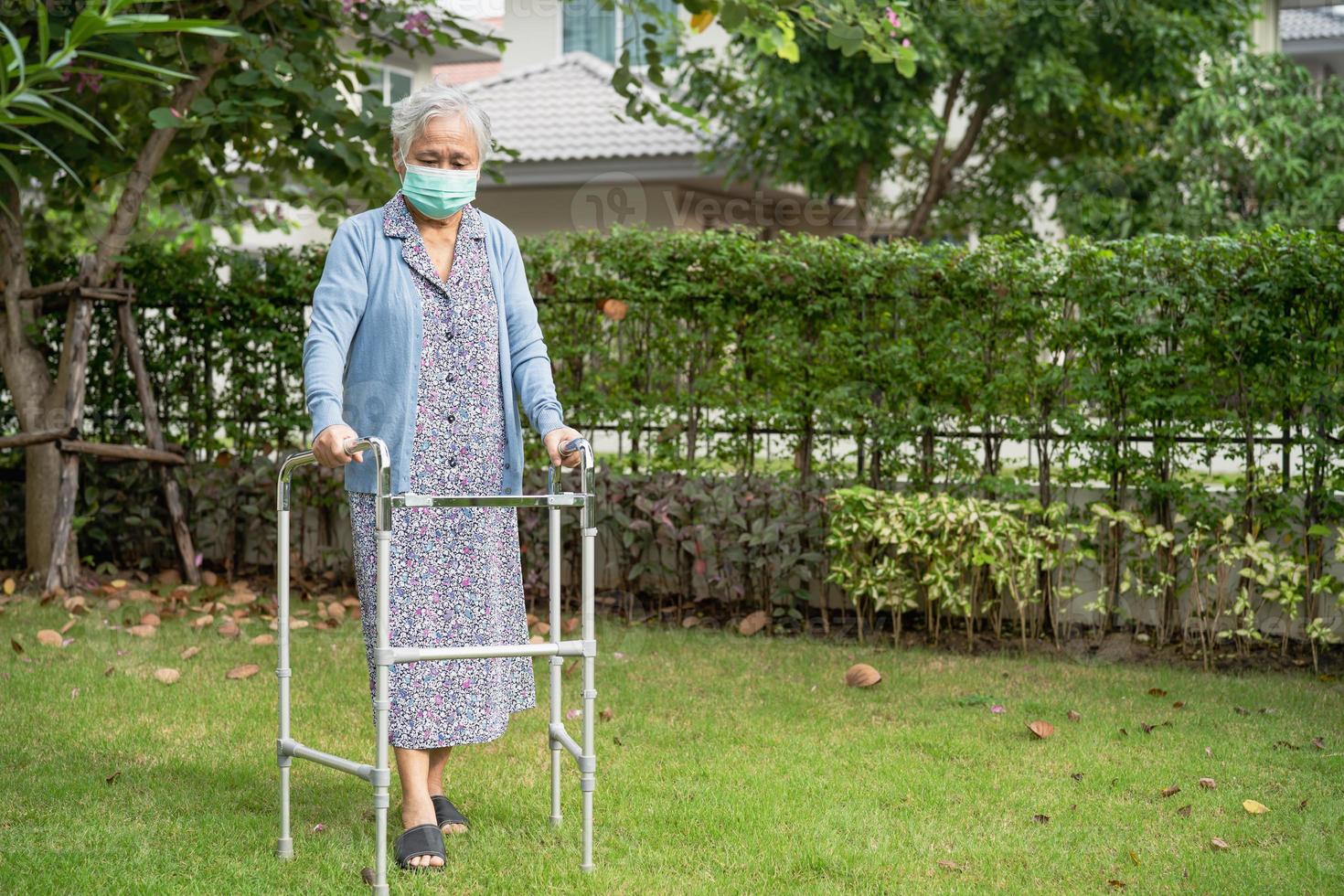 Asian senior or elderly old lady woman walk with walker and wearing a face mask for protect safety infection and kill Novel Coronavirus Covid-19 virus. photo