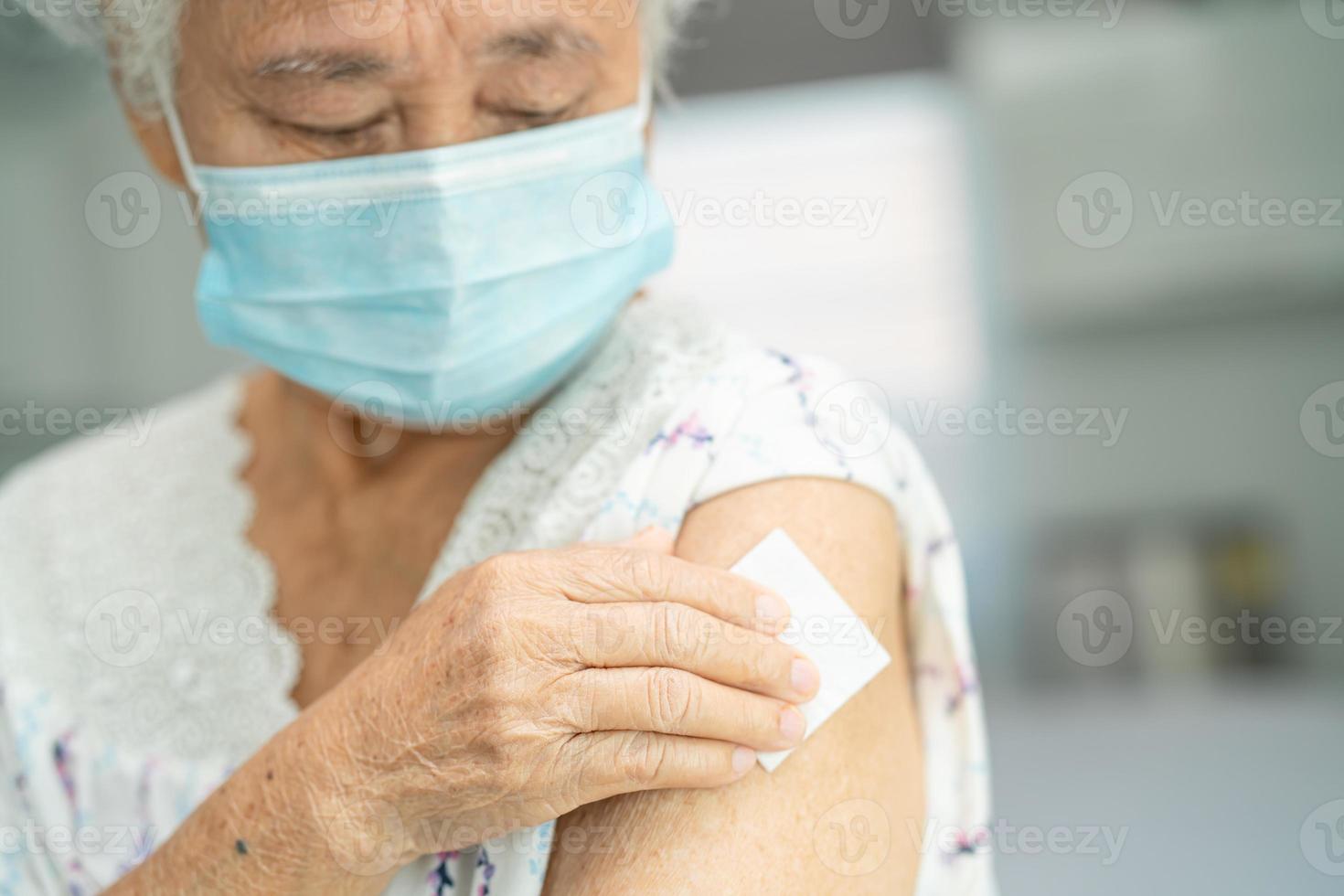 Elderly Asian senior woman wearing face mask getting covid-19 or coronavirus vaccine by doctor make injection. photo