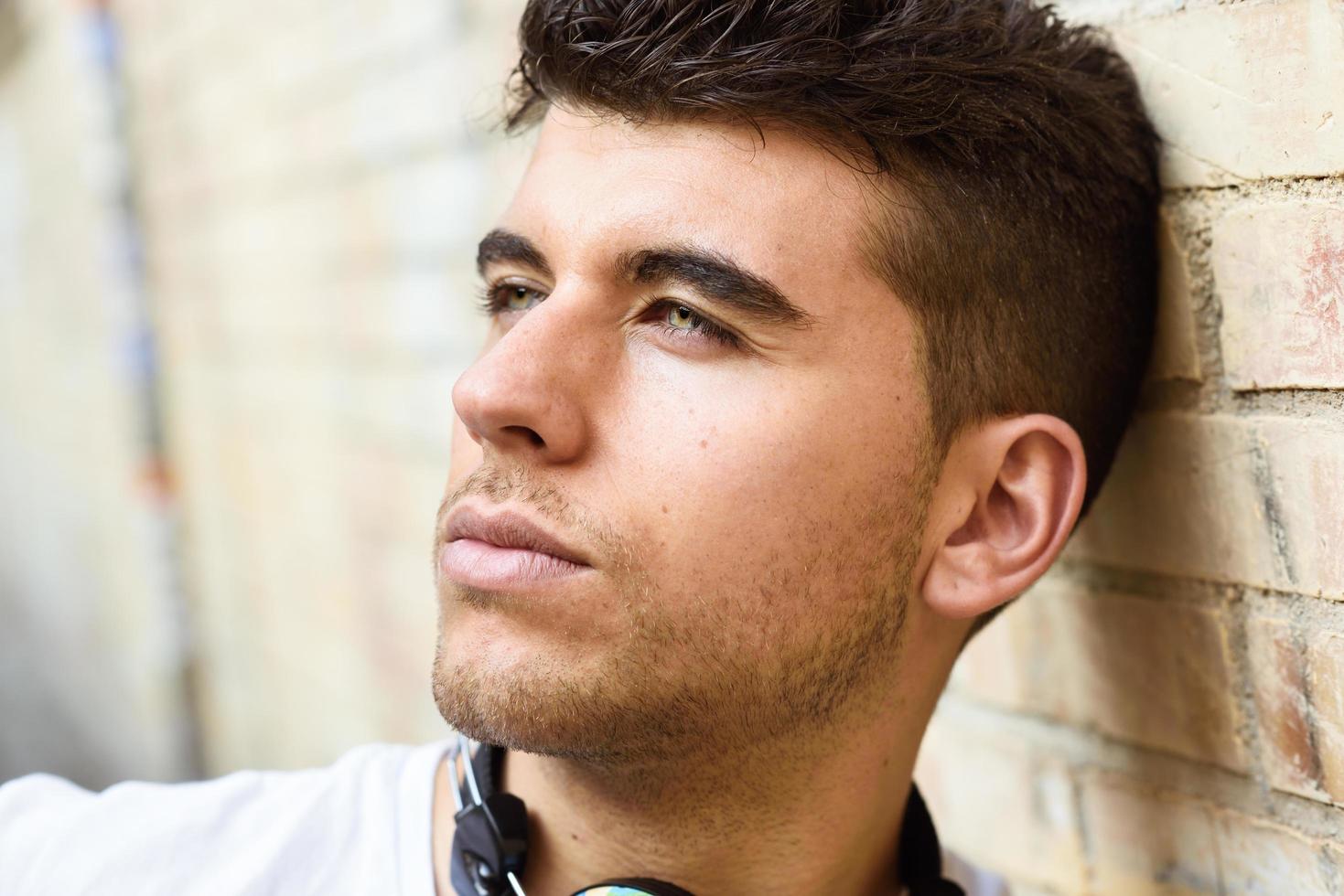 Handsome young man with blue eyes posing near a wall photo