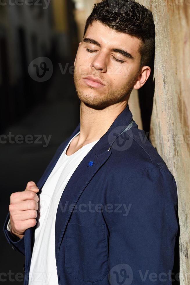 joven guapo con ojos azules posando cerca de una pared foto