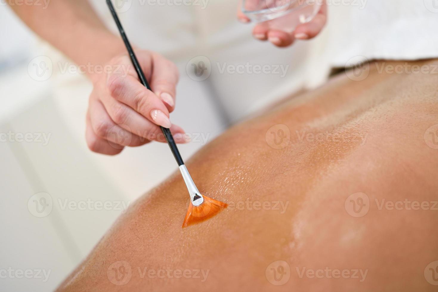 Woman receiving back massage treatment with oil brush photo