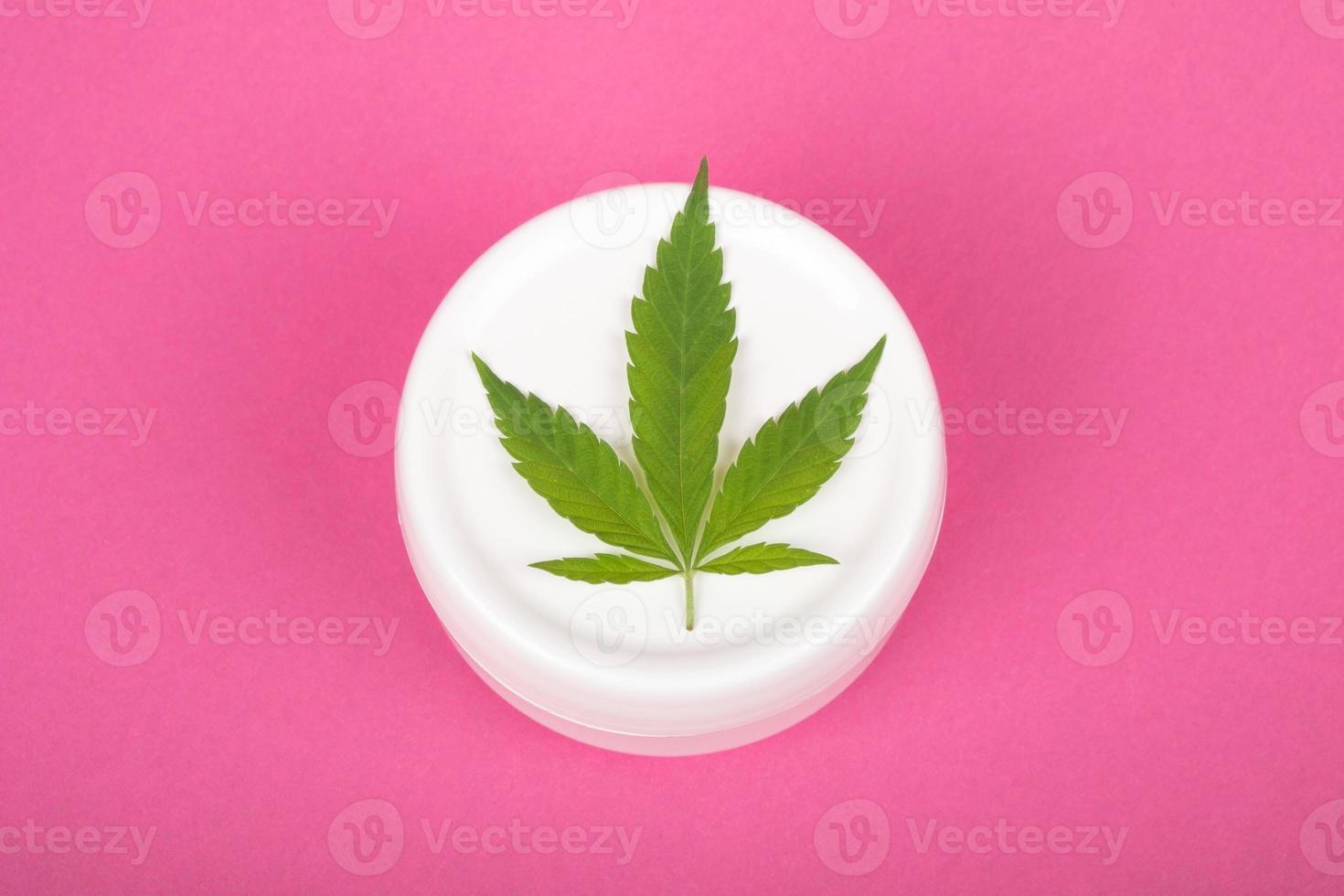 cosmetics with marijuana extract, moisturizer with cannabis leaf on pink background close-up photo