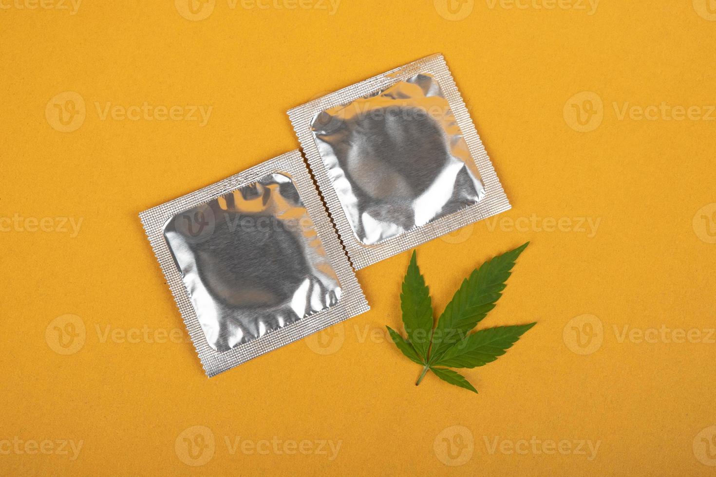 condones y hojas de marihuana sobre un fondo amarillo, sexo y drogas, anticoncepción después del uso de drogas foto