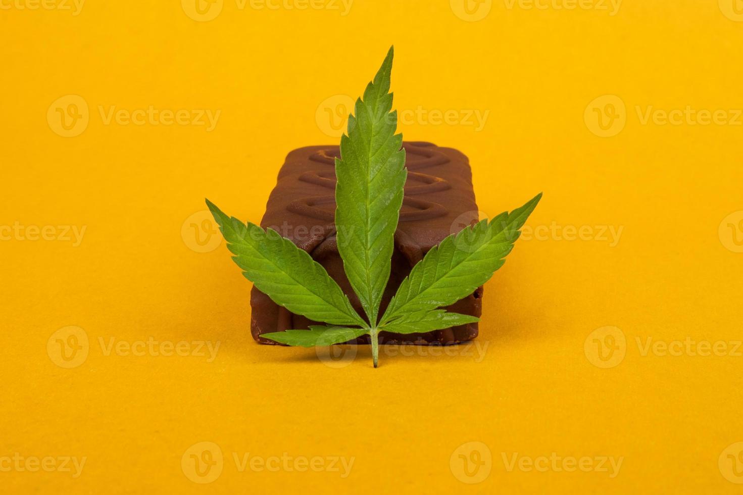caramelos de chocolate y una hoja de marihuana sobre fondo amarillo belleza. caramelos dulces con la adición de aceite de hachís foto