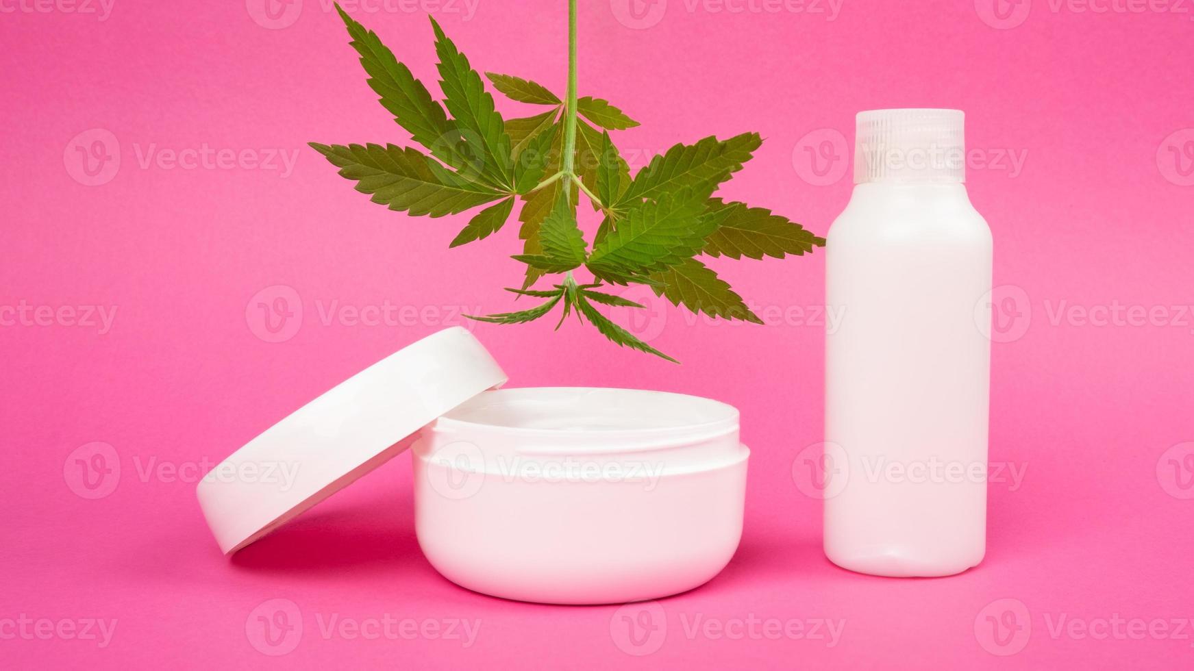 Cosméticos para el cuidado de la piel con extracto de marihuana sobre fondo rosa, crema rejuvenecedora con hoja de cannabis foto