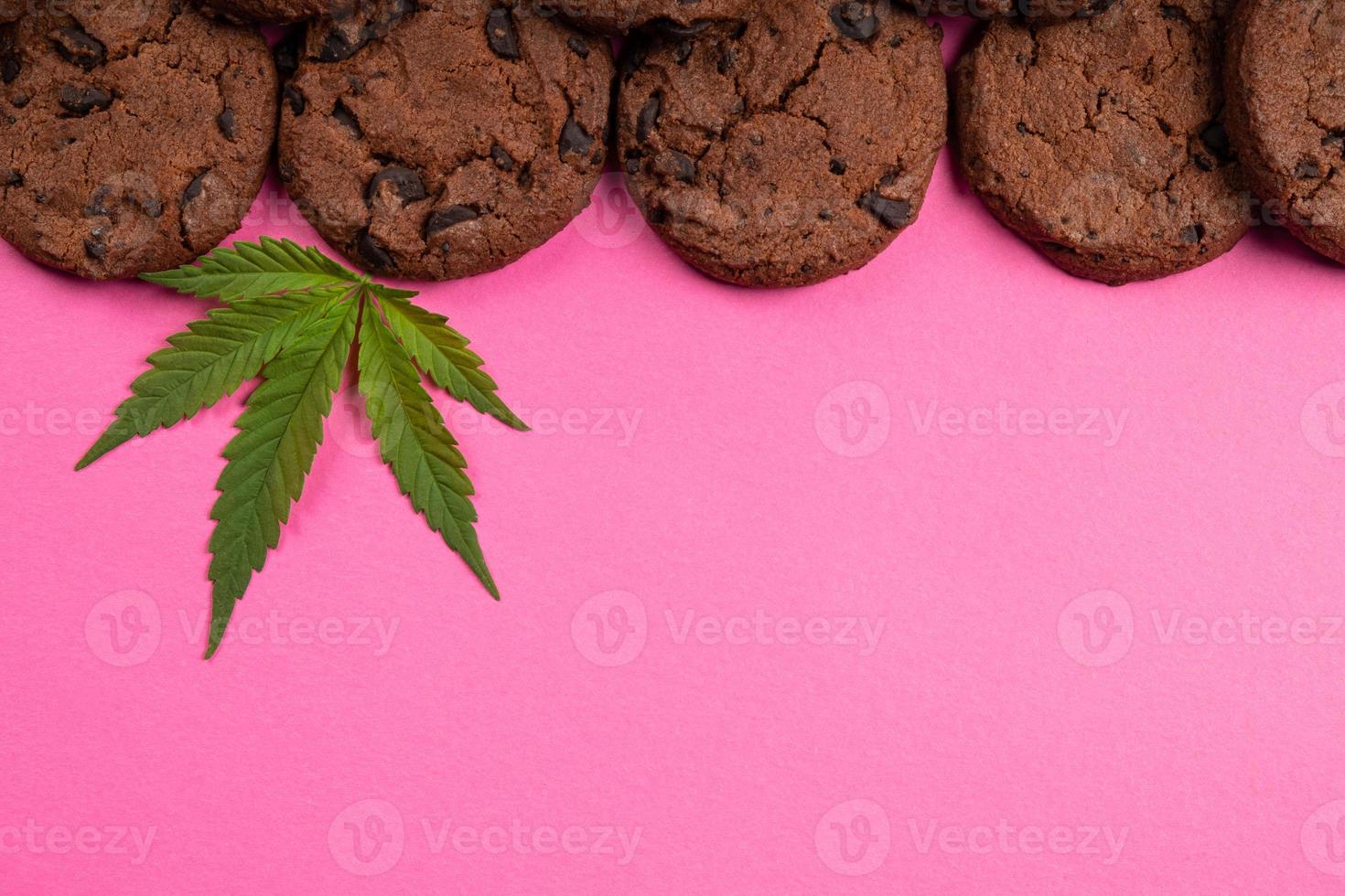 Galleta con chispas de chocolate con hojas de marihuana sobre fondo rosa espacio de copia, dulces con cannabis foto