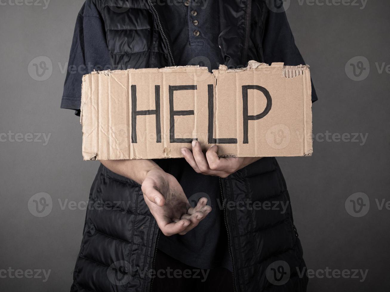 a dirty homeless man stands with a cardboard sign and asks for help photo