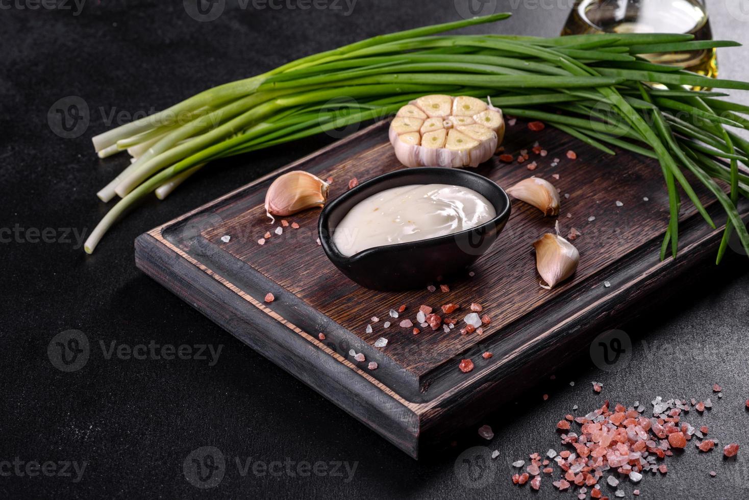 Garlic sauce in a ceramic black sauce with greenery on a wooden cutting board photo