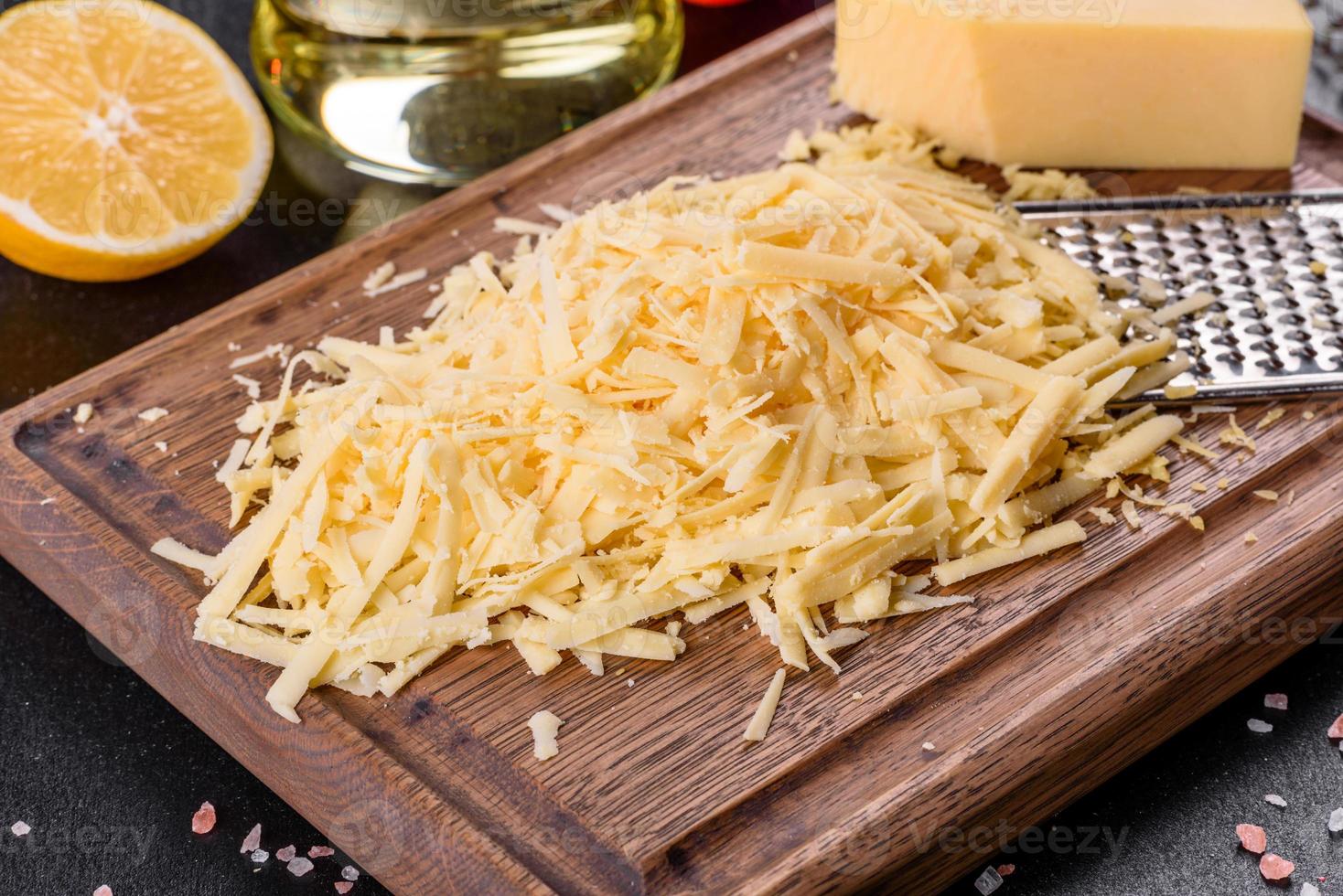 Fresh hard cheese grated on a large grater on a wooden cutting board photo