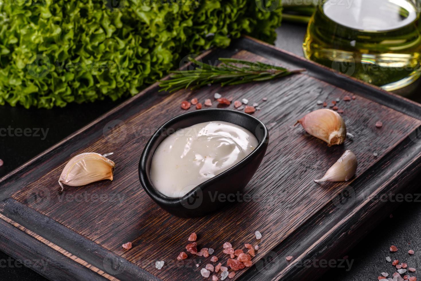 salsa de ajo en una salsa negra de cerámica con vegetación sobre una tabla de cortar de madera foto