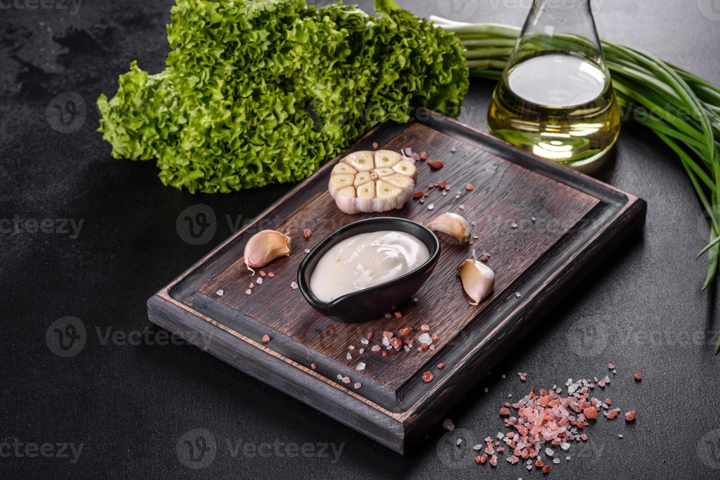 Garlic sauce in a ceramic black sauce with greenery on a wooden cutting board photo