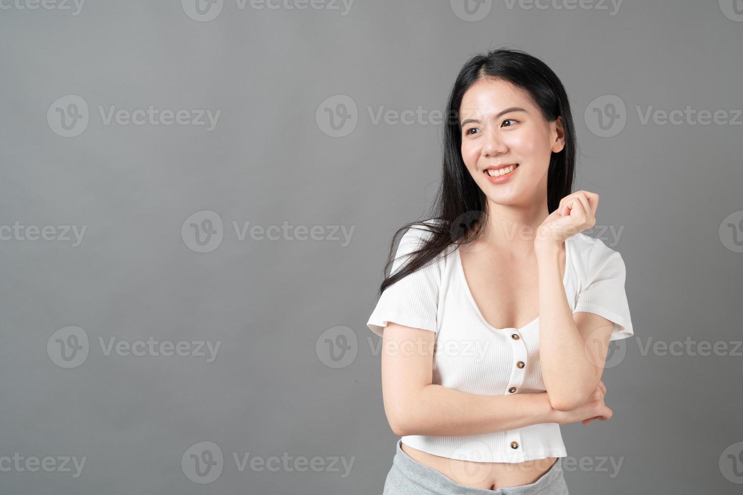 Joven mujer asiática con rostro feliz y sonriente en camisa blanca sobre fondo gris foto