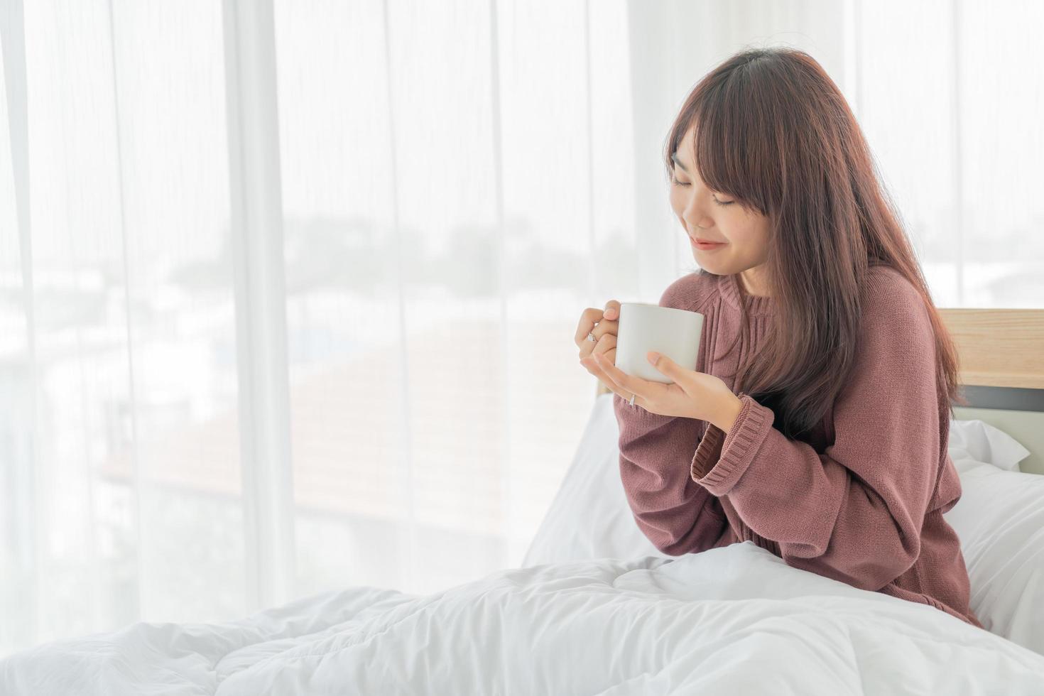 Asian woman drinking coffee on bed in the morning photo