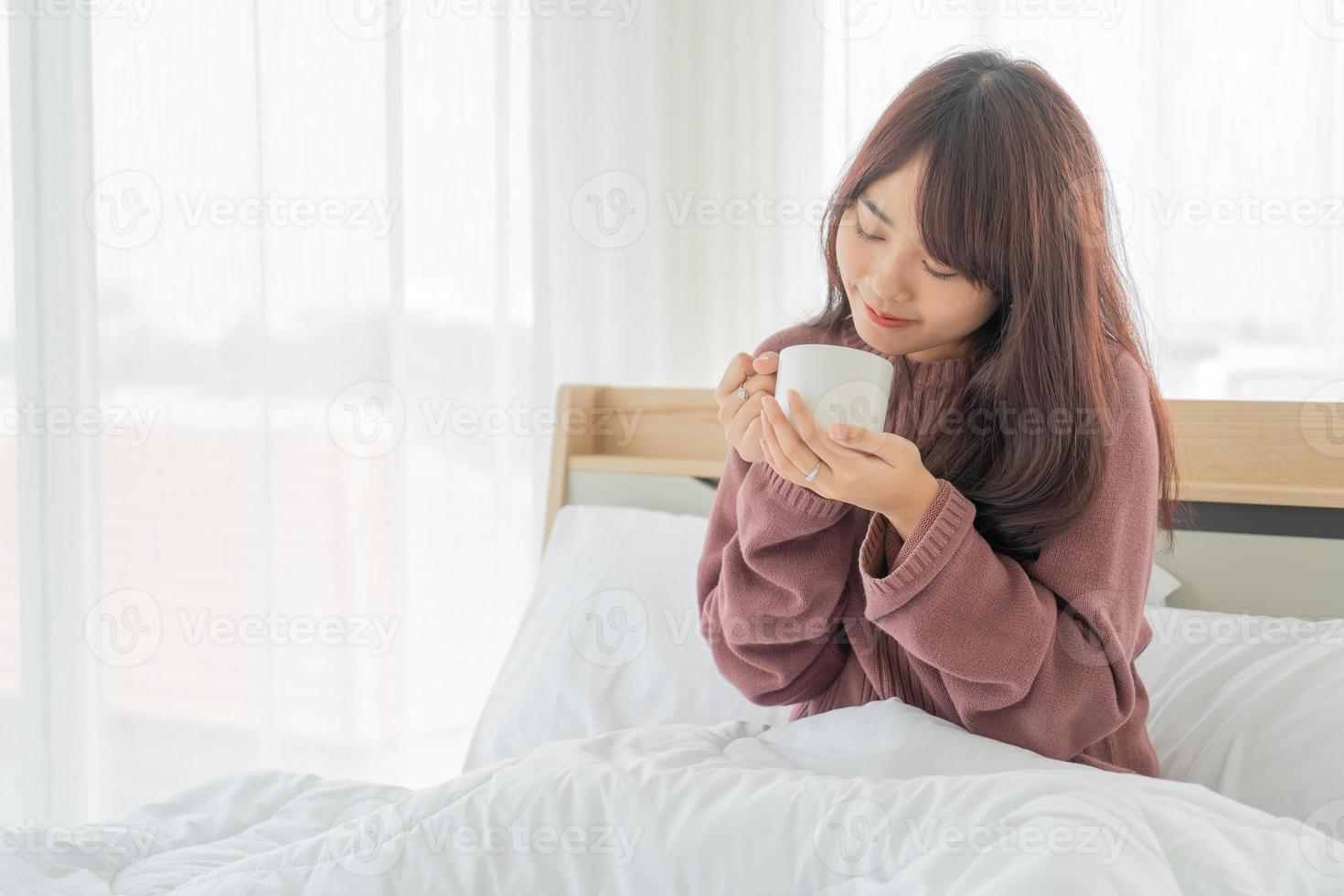 Asian woman drinking coffee on bed in the morning photo