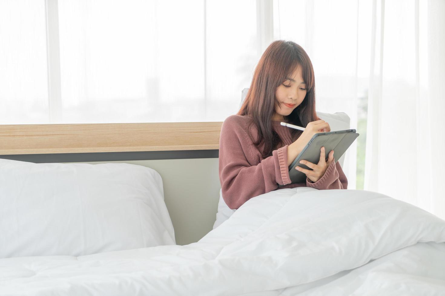 Beautiful Asian woman working with tablet on bed photo