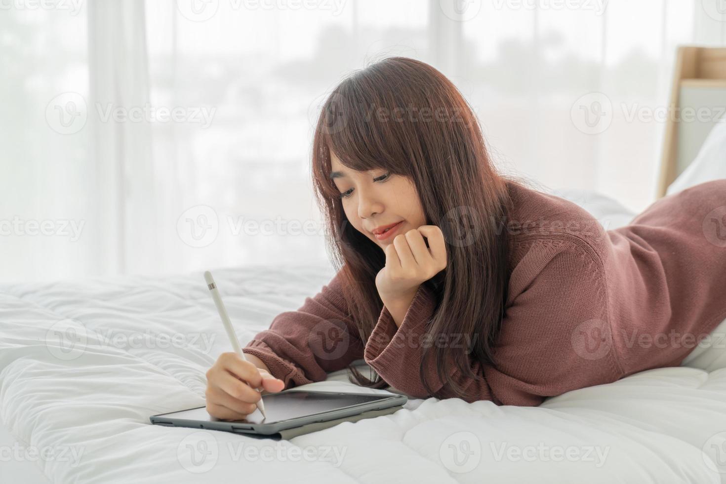 Hermosa mujer asiática que trabaja con la tableta en la cama foto