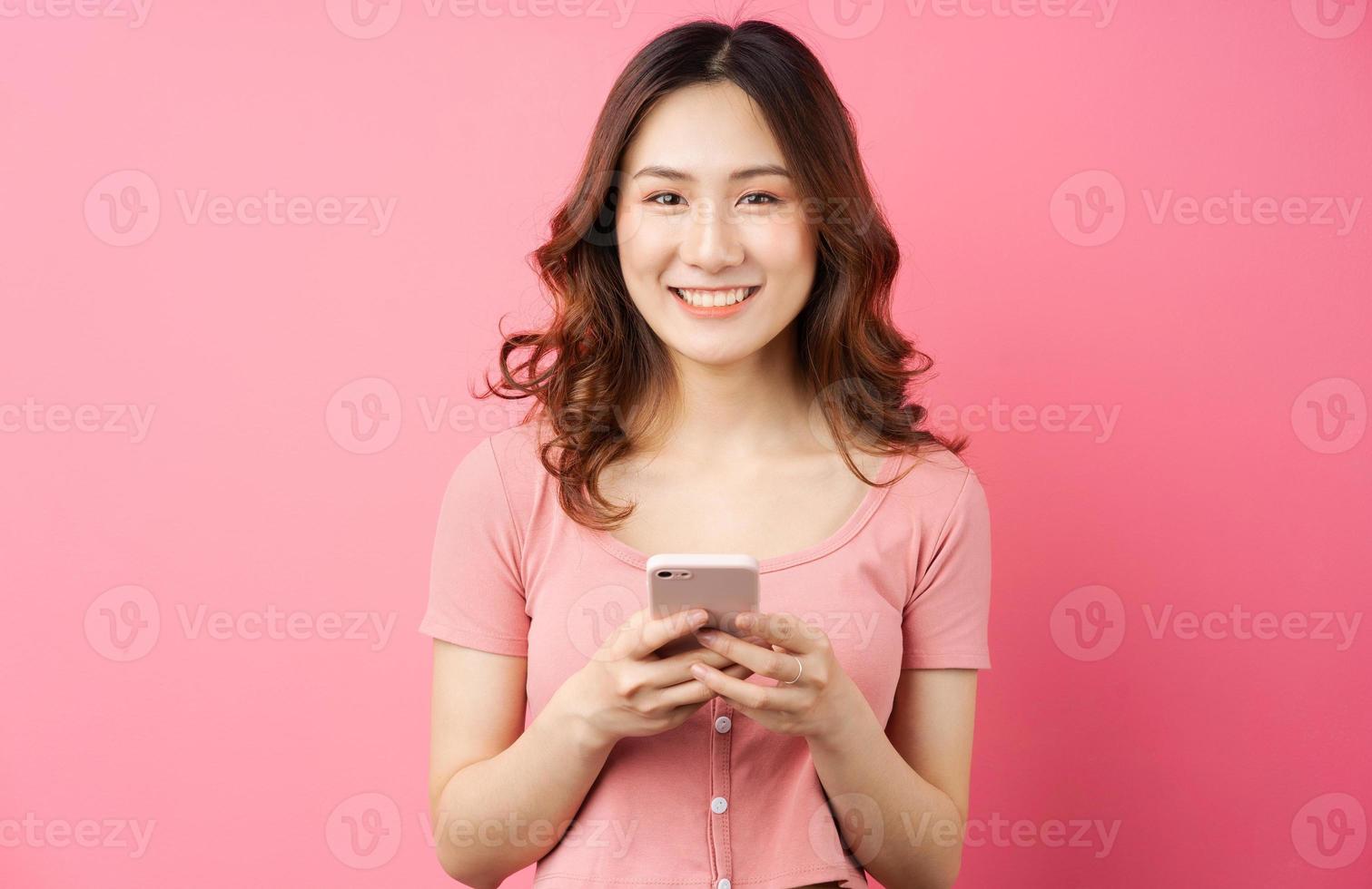 Joven mujer asiática usando el teléfono sobre fondo rosa foto