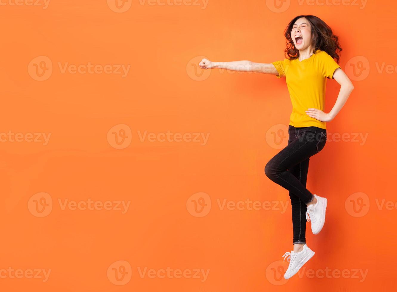 Joven mujer asiática saltando sobre fondo naranja foto