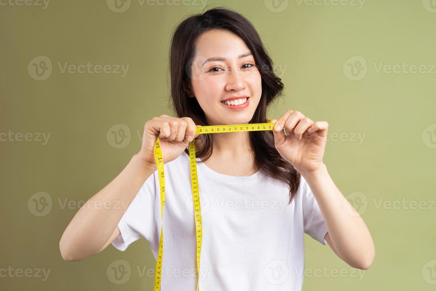 Joven asiática sosteniendo felizmente la cinta métrica después de perder peso foto