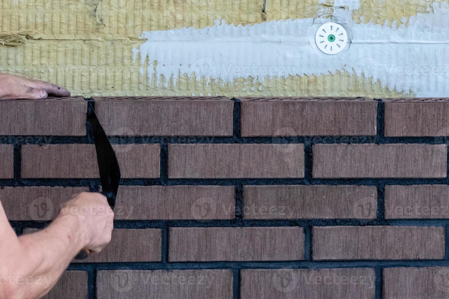 Trabajador de albañil instalando ladrillos en el sitio de construcción. foto