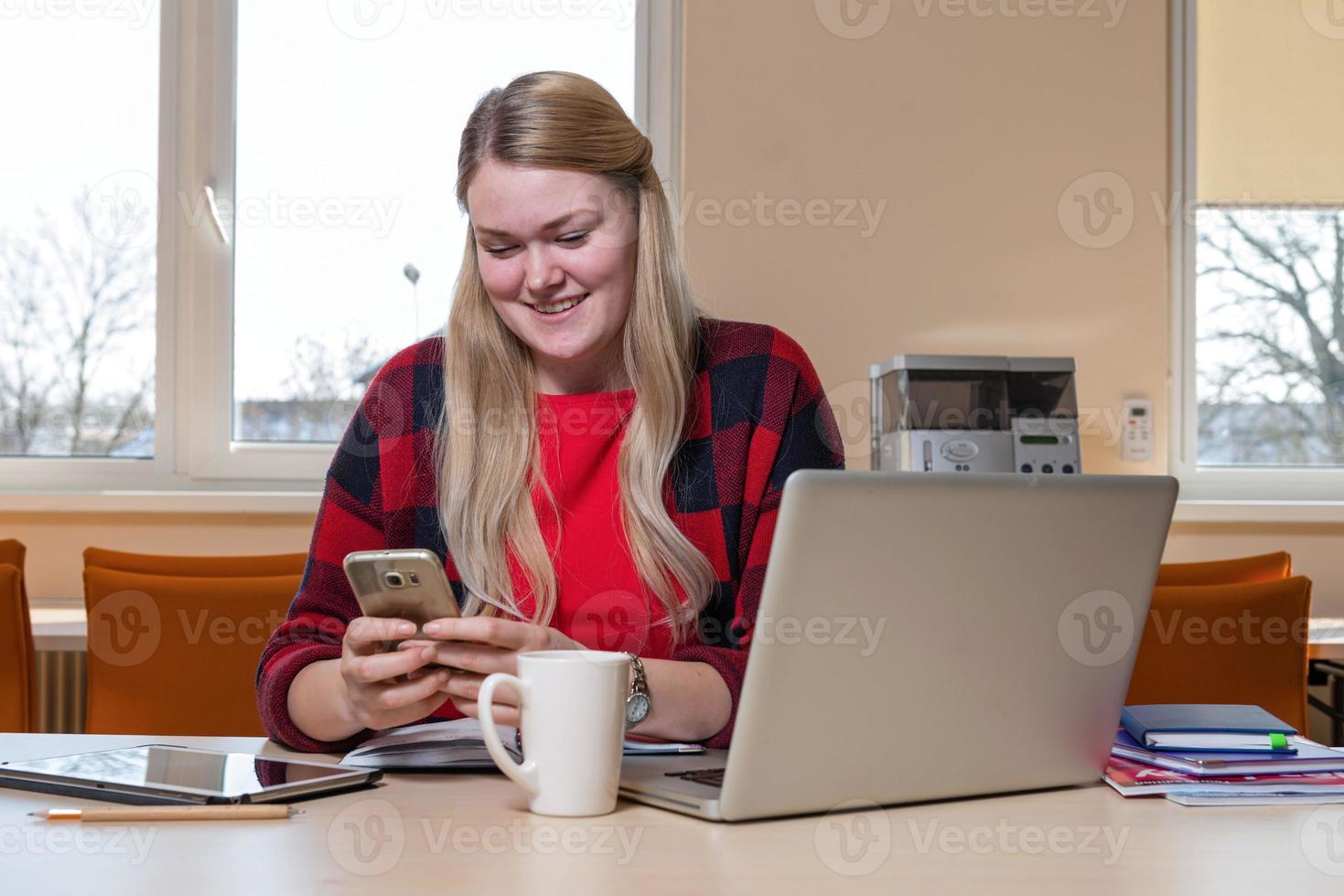 A smiling blonde woman sitting at a laptop and talking over a cell phone. photo
