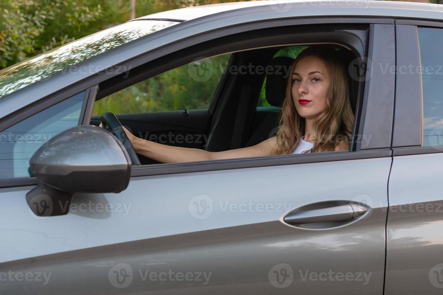 una mujer joven y hermosa con el pelo largo se sienta al volante del coche. foto