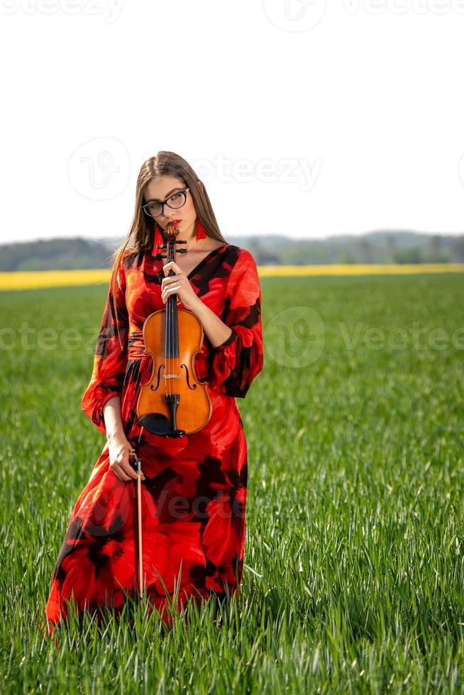 Young woman in red dress with violin in green meadow - image photo