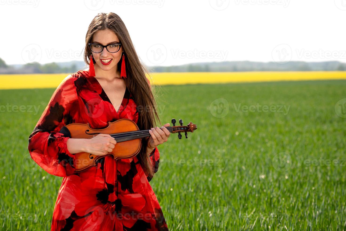 Mujer joven en vestido rojo tocando el violín en la pradera verde - imagen foto