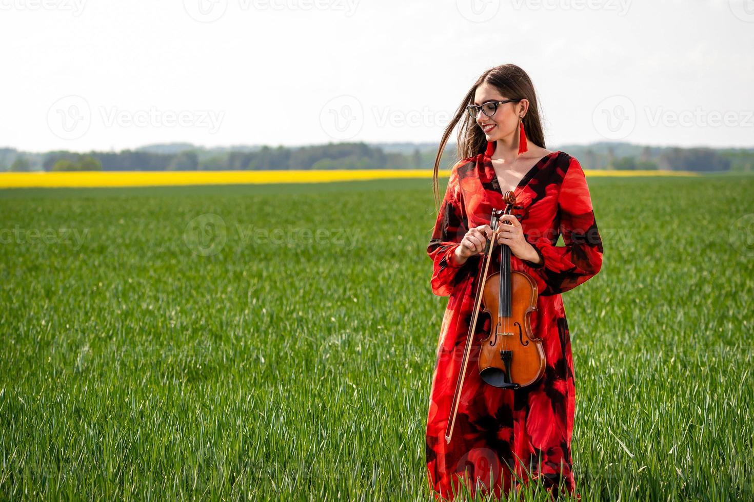 Young woman in red dress playing violin in green meadow - image photo