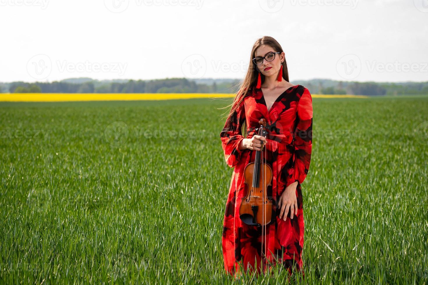 Young woman in red dress playing violin in green meadow - image photo