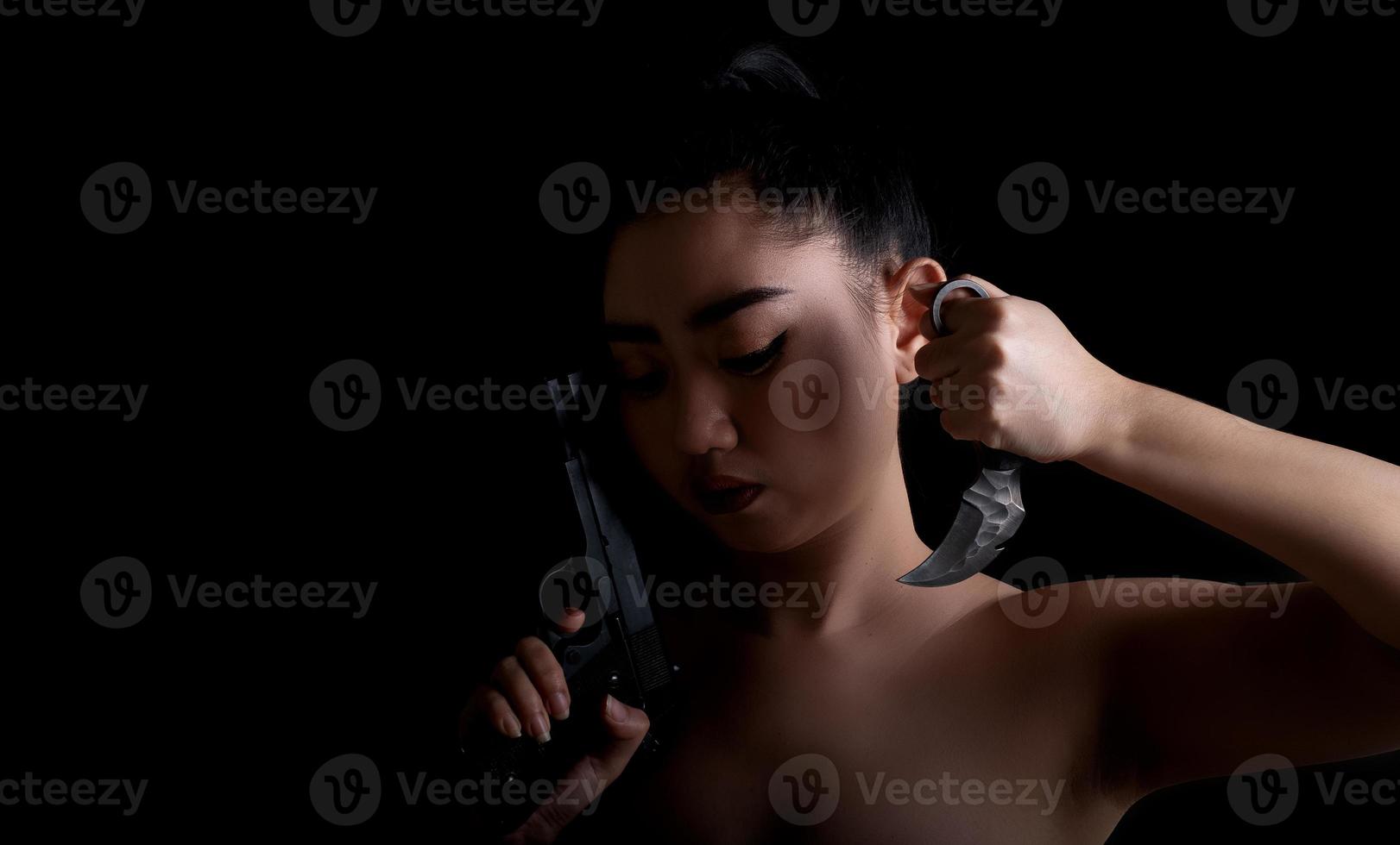 Asia woman one hand holding a gun and karambit knife at the black background photo