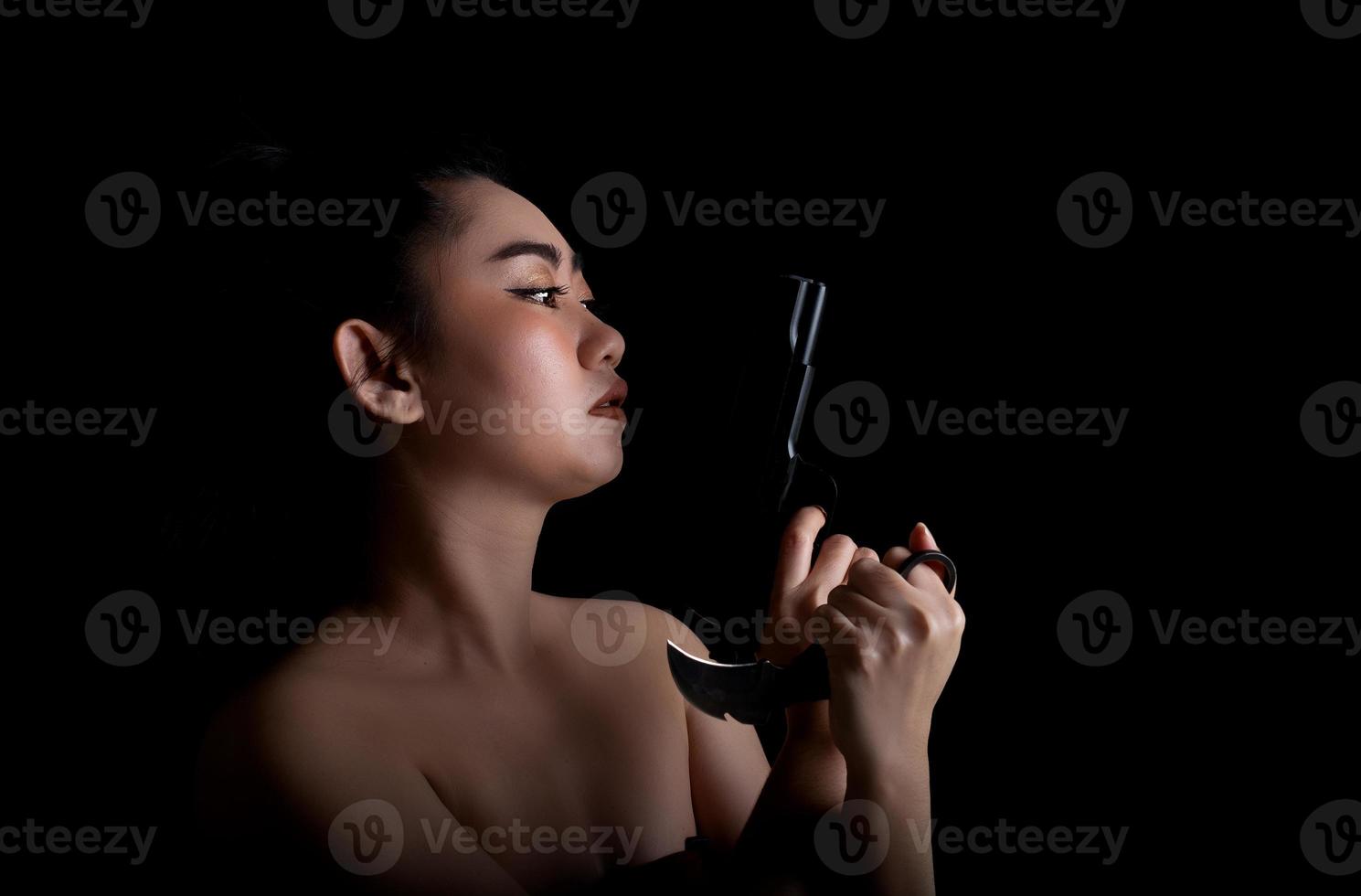 Asia woman one hand holding a gun and karambit knife at the black background photo