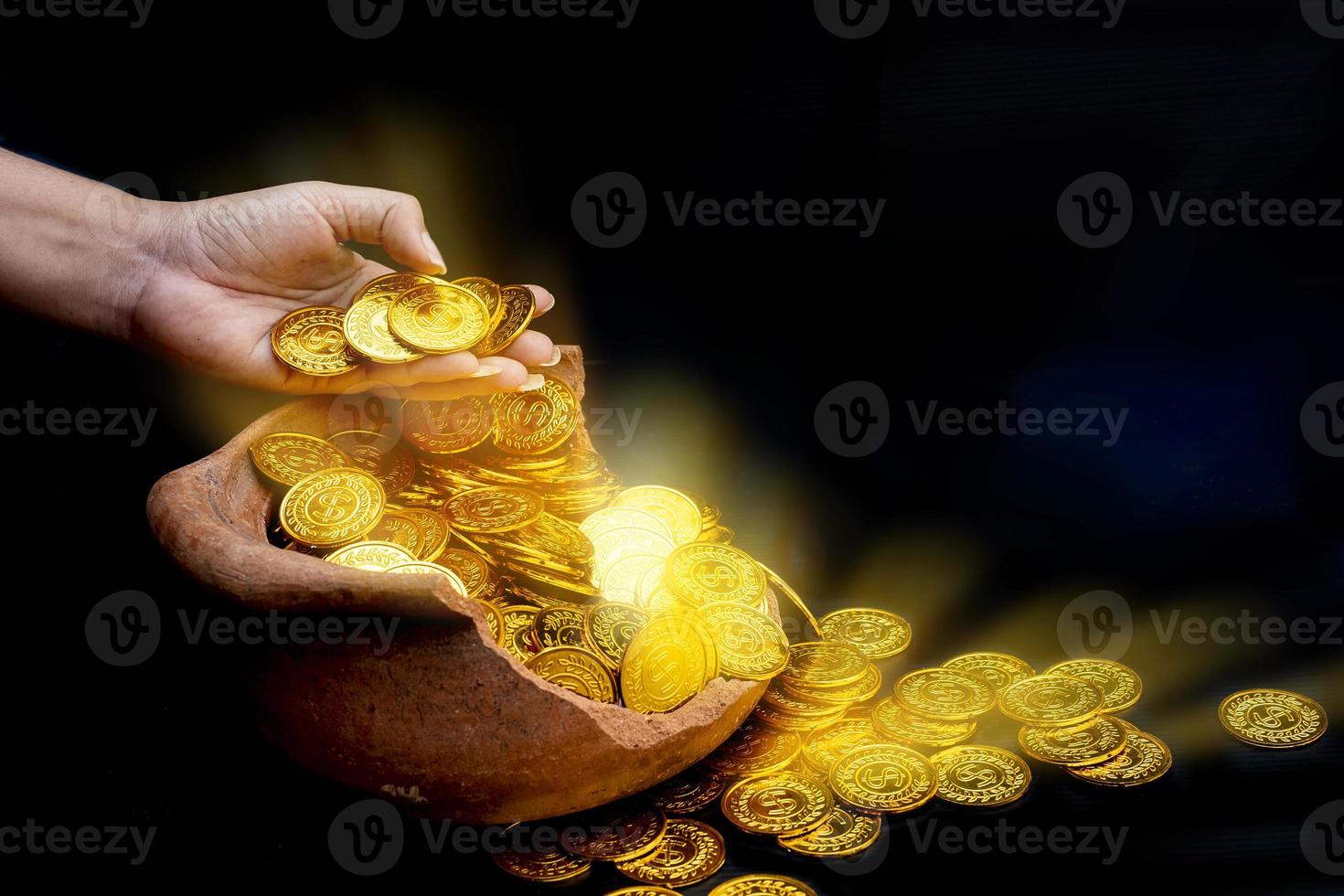 Moneda de oro en la mano en lotes apilando monedas de oro en el frasco del tesoro roto fondo blanco foto